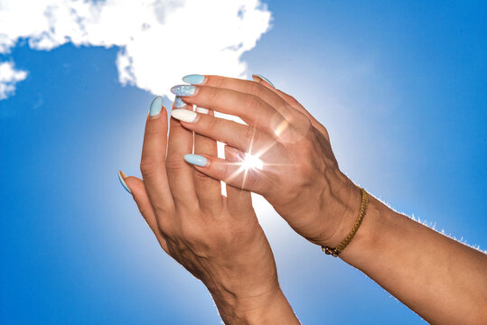Two woman holding hands with white clouds and blue sky background, sun shines through fingers, ray of light