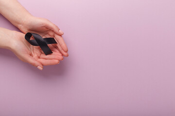 Black awareness ribbon in palms on pink background