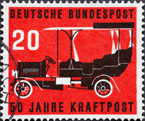 GERMANY - CIRCA 1955: This postage stamp shows shows a post bus from 1906 against a red background....