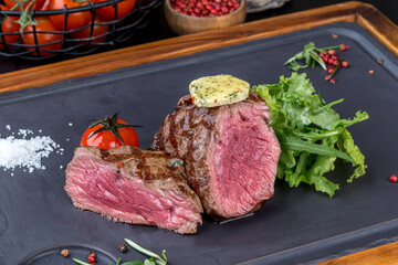 Steak mignon with fresh herbs on a black slate blackboard