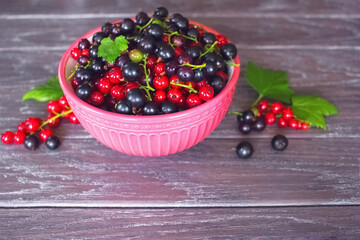 red and black currants in a bowl on a wooden background close-up. background with ripe black and red currant berries.