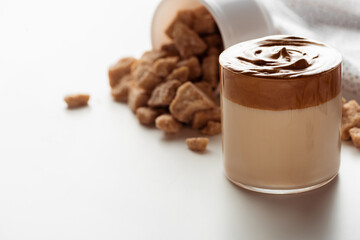 selective focus of delicious Dalgona coffee in glass near scattered brown sugar on white background