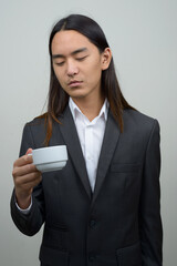 Young Asian businessman with long hair looking at coffee cup