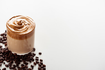 delicious Dalgona coffee in glass near coffee beans on white background