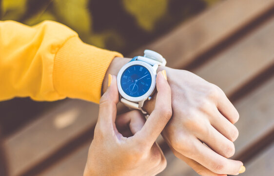 Time. A close-up photo of a smartwatch on a girl's hand, showing time, with two girl's fingers with yellow nails clicking it buttons.