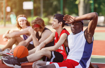 Fototapeta premium Exhausted black basketball player resting with his diverse team at sports court outside