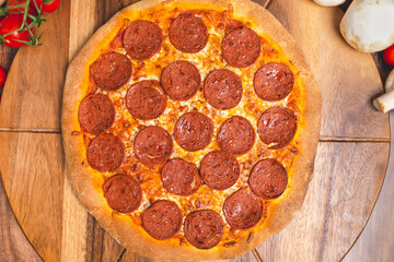 Pepperoni Pizza on a wooden pizza board with lots of ingredients and around. Concept of freshly homemade pizza with a lot of pepperoni salami on the top with free space for your text/decoration. 