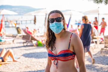 Young woman wearing medical mask at the beach. New normal concept.