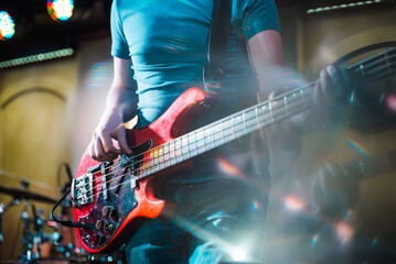 Obraz premium The musician plays the electric bass guitar on stage. Guitar neck close-up on a concert of rock music in the hands of a musician. Fingers on fretboard