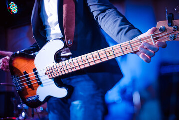 The musician plays the electric bass guitar on stage. Guitar neck close-up on a concert of rock music in the hands of a musician