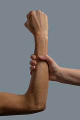 Close-up of light-skinned hand clenching dark-skinned forearm