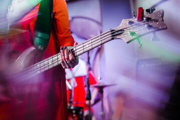 Fototapeta premium The musician plays the electric bass guitar on stage. Guitar neck close-up on a concert of rock music in the hands of a musician