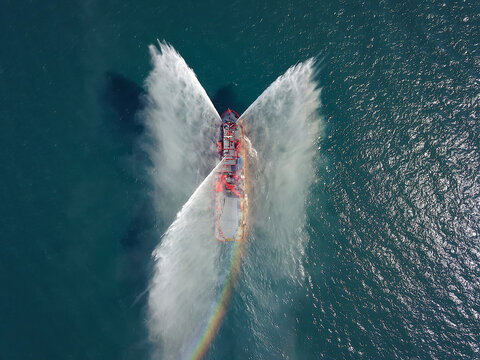 A Floating Modern Ship Sprays Jets Of Water, Demonstrates Fire Fighting Water Cannon, Sprays Water As Firefighter Boat Top View From The Drone