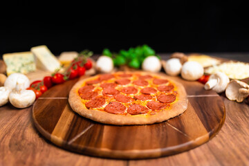 Pepperoni Pizza on a wooden pizza board with lots of ingredients and around. Concept of freshly homemade pizza with a lot of pepperoni salami on the top with free space for your text/decoration. 