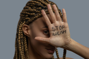 Young African American woman covering her one eye with palm with stop racism lettering