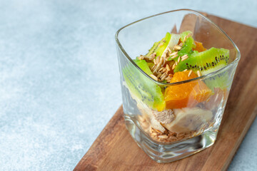 Glass with fruit pieces and oatmeal muesli on wooden board