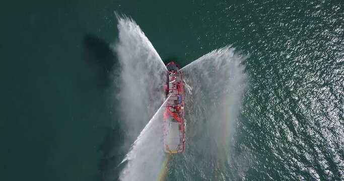 A floating modern ship sprays jets of water, demonstrates fire fighting water cannon, sprays water as firefighter boat top view from the drone
