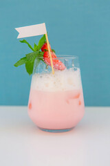 strawberry cocktail in front of a white background. cold pink cocktail with ice on the beach club in hot summer day. cocktail image with foam on the background with white and blue floor.