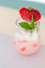 strawberry cocktail in front of a white background. cold pink cocktail with ice on the beach club in hot summer day. cocktail image with foam on the background with white and blue floor.