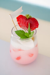 strawberry cocktail in front of a white background. cold pink cocktail with ice on the beach club in hot summer day. cocktail image with foam on the background with white and blue floor.