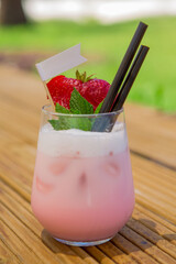 strawberry cocktail in front of a white background. cold pink cocktail with ice on the beach club in hot summer day. cocktail image with foam on the background with wooden floor and green leaves.