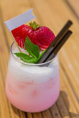 strawberry cocktail in front of a white background. cold pink cocktail with ice on the beach club in hot summer day. cocktail image with foam on the background with wooden floor and green leaves.