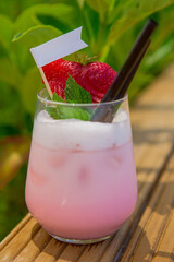 strawberry cocktail in front of a white background. cold pink cocktail with ice on the beach club in hot summer day. cocktail image with foam on the background with wooden floor and green leaves.