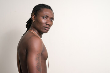 Stressed young muscular African man with dreadlocks looking back shirtless