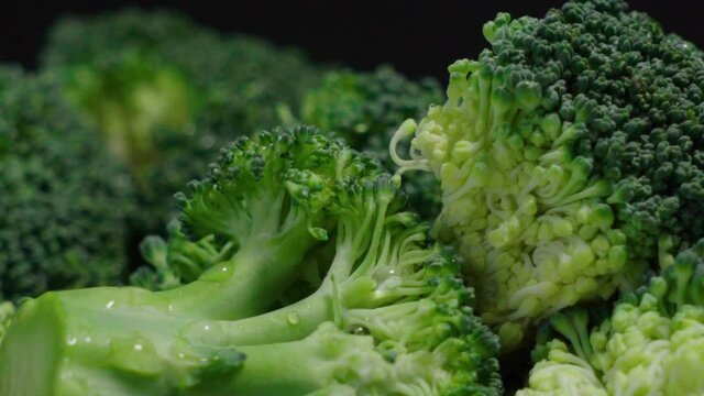 Closeup Tilt Down of Broccoli Pieces with Water Droplets on Black Background