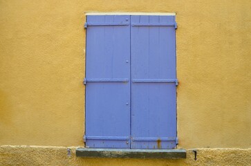 Purple closed wooden shutters in a yellow house wall, Provence, France