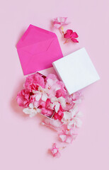 Pink envelope and gift box full of flowers  over a pink background