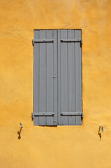 Grey closed wooden shutters in a yellow house wall in Provence, France