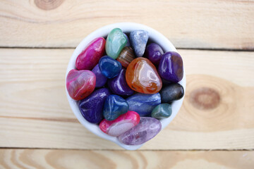Multi-colored semi-precious stones in a ceramic mortar on a wooden table.