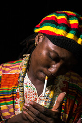 Face of young African Rastafarian man lighting cigarette outdoors at night