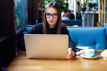 Pensive brunette copywriter in eyewear searching information in network for publication working on...
