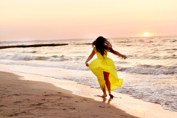 A girl in a yellow dress with long hair runs along the seashore at dawn.