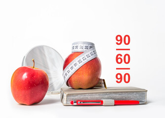 Диета. Dieting. Diet. Red Apples tied with diet measuring tape, stands on a notepad in front of a mirror. Female body types. Composition isolated on white background. Red apple. 90/60/90