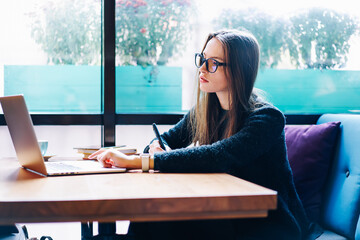 Attractive skilled female copywriter searching information for creating publications in cafe...