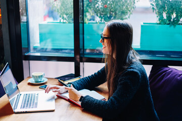 Positive brunette hipster girl using laptop for watching funny videos from network resting on...
