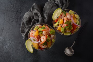 Ceviche salad with shrimps, oranges and avocado in glass bowl on a dark or grey background. Latin...
