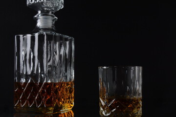 Glass of the whiskey with ice cubes and a square decanter on a black  background.