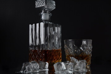 Glass of the whiskey with ice cubes and a square decanter on a black  background.