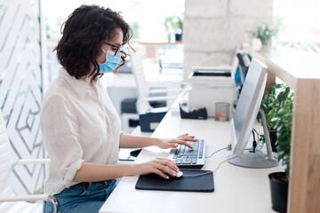 Obraz na płótnie Canvas Worker wearing protective mask at hotel reception. Protection employees on safe workplace. Young woman working in office as receptionist. Social distance during coronavirus quarantine, staff safety.