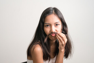 Young beautiful Asian teenage girl sitting and using hair as mustache