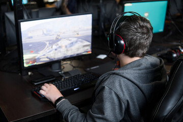 POLAND, WARSAW - June 10, 2020: Back view of young gamer in headphone playing video game at computer club.