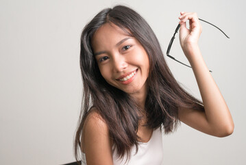 Happy young beautiful Asian teenage girl sitting and holding eyeglasses