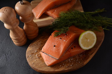 Fresh raw salmon fish fillet with cooking ingredients, herbs and lemon on black background. Keto...