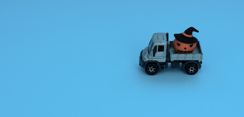 The grey truck car is carrying an orange decorative pumpkin on blue background. Halloween, minimalism concept. Greeting, invitation card. Wide banner for copy space.