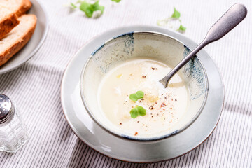 Cauliflower and Potato Cream Soup served with herbs and pepper on white linen striped tablecloth. Selective focus