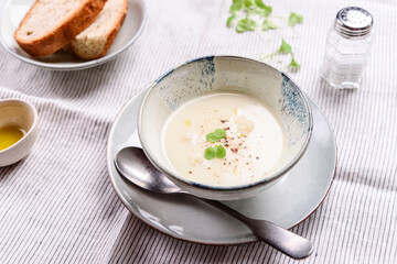 Cauliflower and Potato Cream Soup served with herbs and pepper on white linen striped tablecloth. Selective focus
